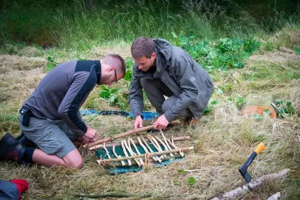 Zwei Personen bauen eine selbstgebaute Konstruktion aus Ästen auf einer Wiese