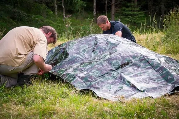 Zwei Personen bauen eine Tarp-Notunterkunft im Gras auf
