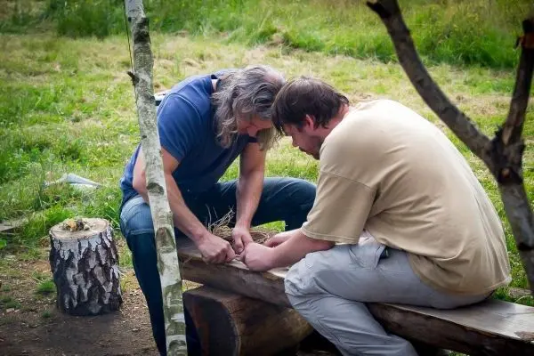 Zwei Personen bearbeiten gemeinsam ein Holzstück auf einer Bank