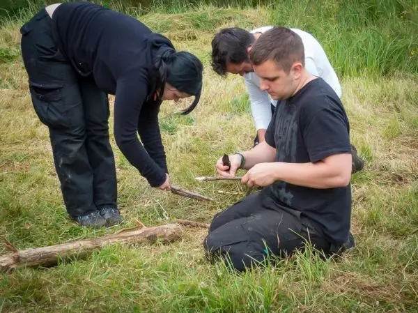 Zwei Personen bearbeiten Holzstücke, während eine dritte mit einem Messer arbeitet