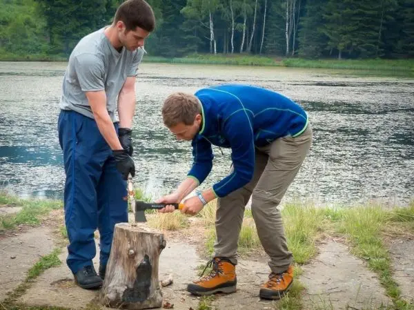 Zwei Personen hacken Holz auf einem Baumstumpf am Wasser