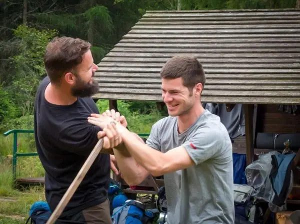 Zwei Personen halten einen langen Stock und üben eine Technik