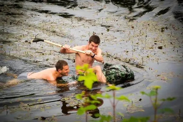 Zwei Personen im Wasser, eine mit einem Paddel, ziehen einen großen Sack