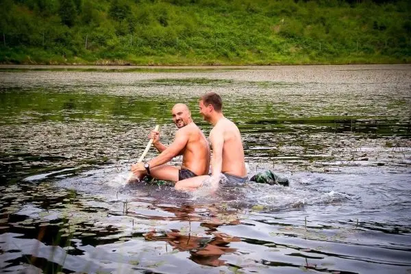 Zwei Personen paddeln auf einem improvisierten Floß über einen ruhigen See