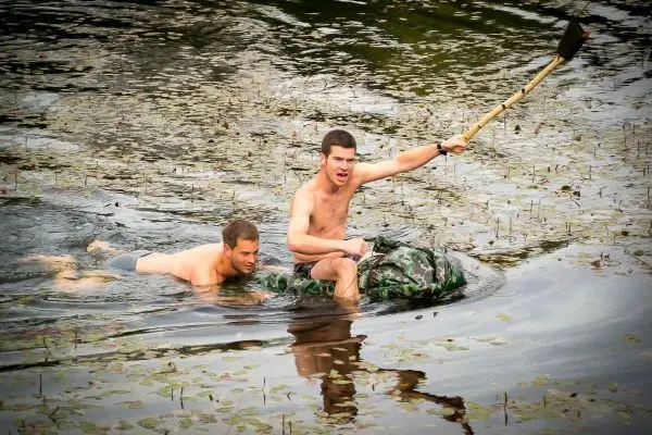 Zwei Personen schwimmen in einem Gewässer, einer hält einen Stock hoch