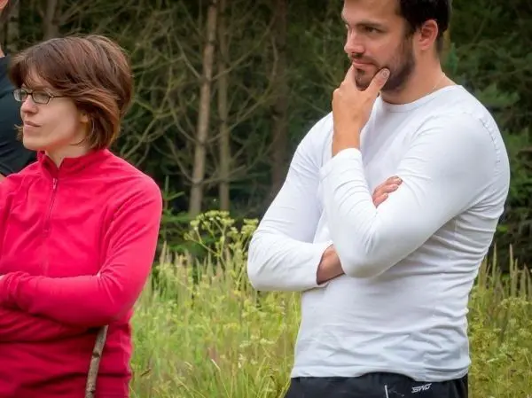 Zwei Personen stehen in einer Wiese, eine hält einen Stock