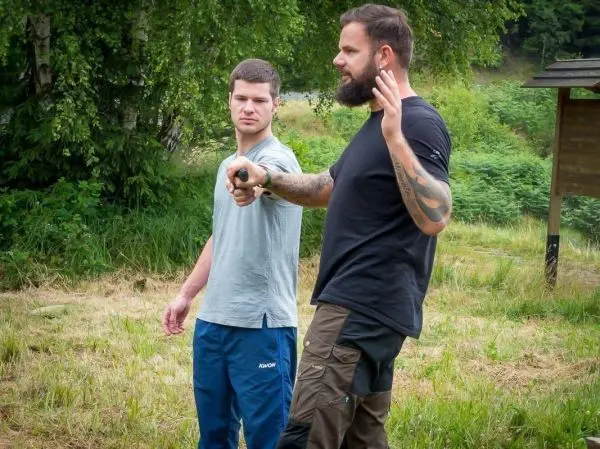 Zwei Personen stehen in einer Wiese, eine Person zeigt gestikulierend auf etwas