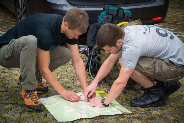 Zwei Personen studieren eine Karte auf dem Boden, Rucksäcke im Hintergrund