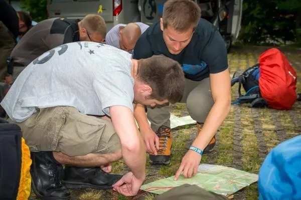Zwei Personen studieren eine Karte auf dem Boden, während Rucksäcke im Hintergrund liegen