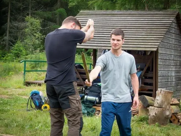Zwei Personen üben den Umgang mit einem Stock in der Nähe einer Holzunterkunft