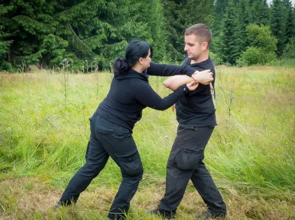 Zwei Personen üben eine Selbstverteidigungstechnik in einem grasbewachsenen Feld