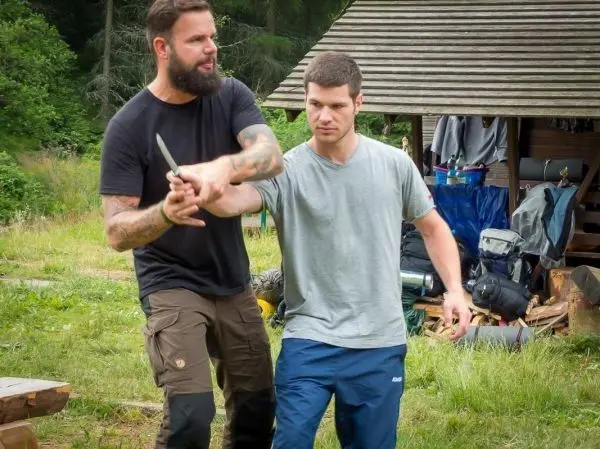 Zwei Personen üben eine Technik mit einem Messer in einer Waldumgebung