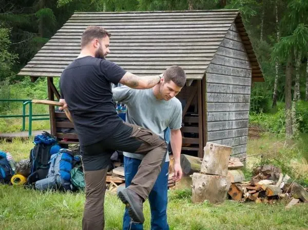 Zwei Personen üben eine Technik zur Selbstverteidigung in der Nähe einer Holzhütte