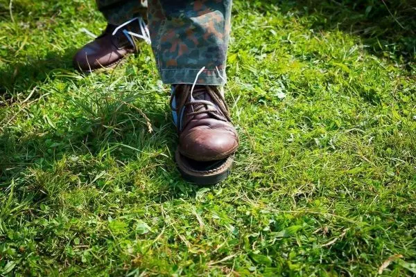 Braune Stiefel stehen auf grünem Gras, Schnürsenkel sind locker