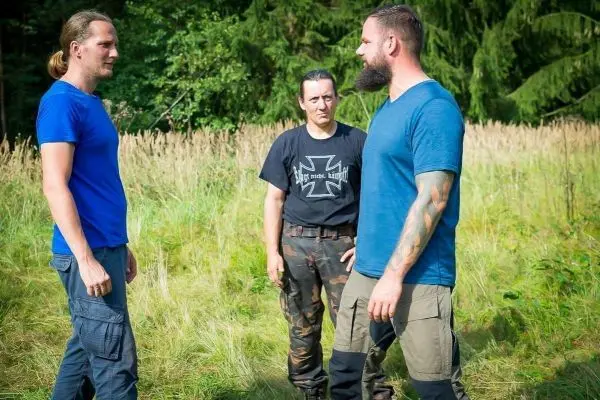 Drei Personen stehen in einer Wiese und diskutieren miteinander