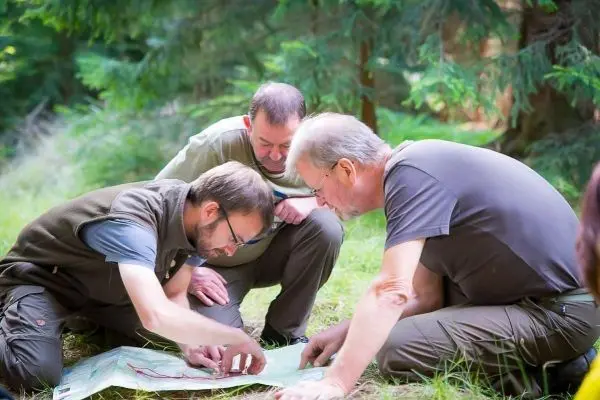 Drei Personen studieren eine Karte auf dem Boden im Wald