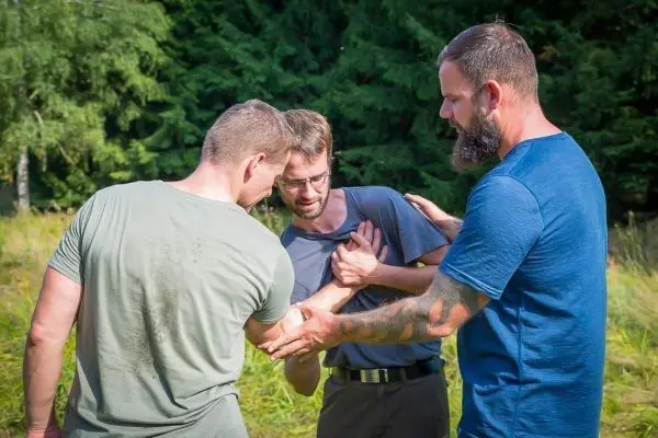 Drei Personen unterstützen einen Mann, der sich am Oberkörper fasst