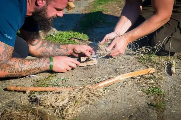 Feuerstahl erzeugt Funken auf Zunder während zwei Personen gemeinsam arbeiten
