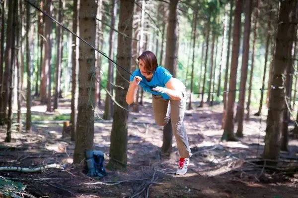 Frau überquert selbstgebaute Seilbrücke zwischen Bäumen im Wald