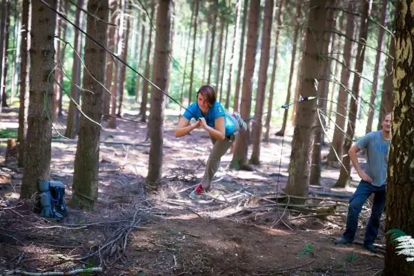 Frau überquert selbstgebaute Seilbrücke zwischen Bäumen im Wald
