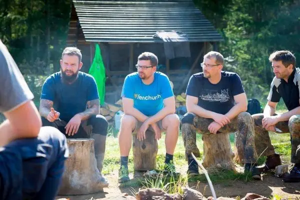 Fünf Männer sitzen auf Baumstümpfen und diskutieren am Lagerfeuer