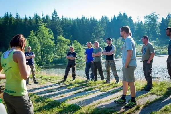 Gruppe steht am Ufer eines Gewässers und hört einer Person zu