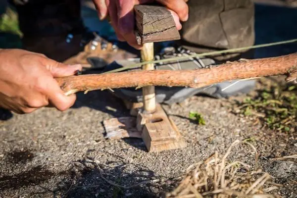 Holzstück wird mit einem anderen Stock bearbeitet, um Feuer zu erzeugen