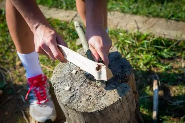 Holzstück wird mit einem Messer bearbeitet auf einem Baumstumpf