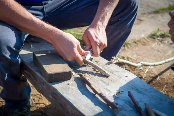 Holzstück wird mit einem Messer bearbeitet, Späne fallen auf eine Holzbank