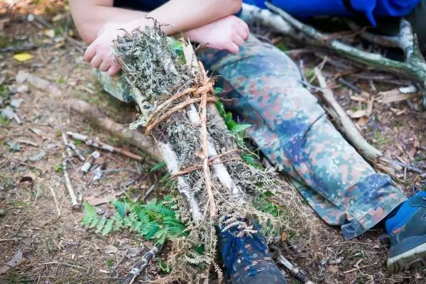Improvisierte Schiene aus Ästen und Moos zur Stabilisierung eines verletzten Beins