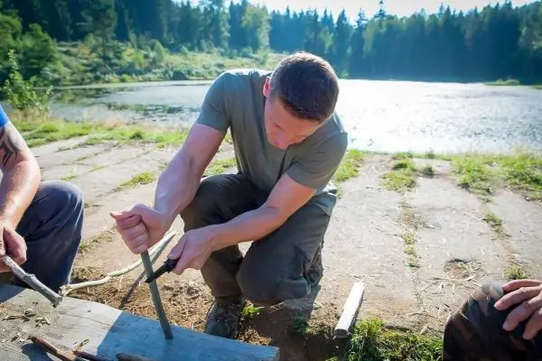 Mann bearbeitet Holzstück mit einem Messer auf einer Holzplatte