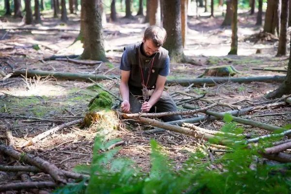 Mann bearbeitet Holzstücke auf dem Waldboden mit einem Messer