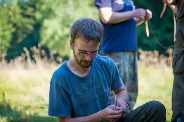 Mann bearbeitet mit einem Messer ein Stück Holz im Freien