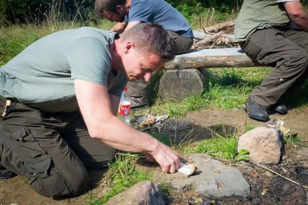 Mann bearbeitet Zunder mit einem Messer auf dem Boden
