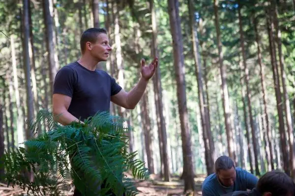 Mann erklärt eine Technik im Wald, während andere Teilnehmer am Boden arbeiten