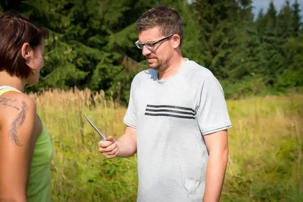 Mann hält ein Messer in der Hand und spricht mit einer Frau im Freien