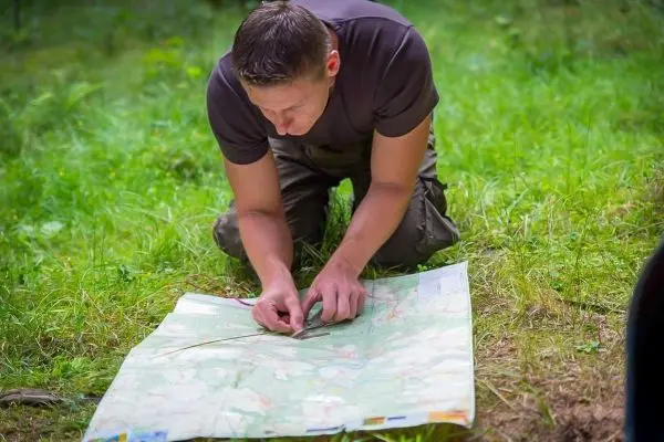 Mann kniet auf dem Boden und studiert eine Karte im Gras