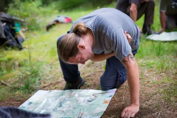 Mann kniet auf dem Boden und studiert eine Karte im Wald