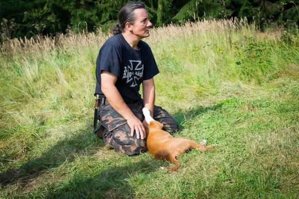 Mann kniet im Gras und streichelt einen Hund