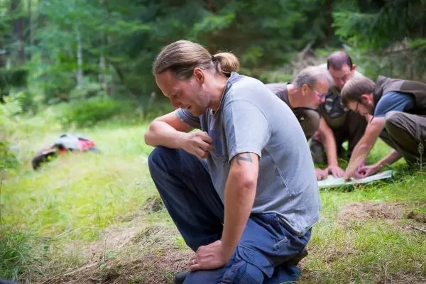Mann kniet im Gras, während andere Teilnehmer eine Karte studieren