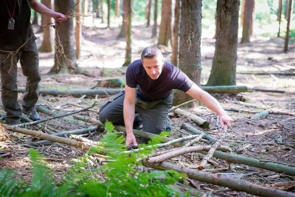 Mann kniet im Wald und sortiert Äste auf dem Boden