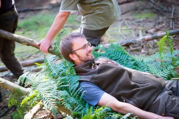 Mann liegt auf einem Bett aus Farnen und Holzstöcken in der Natur