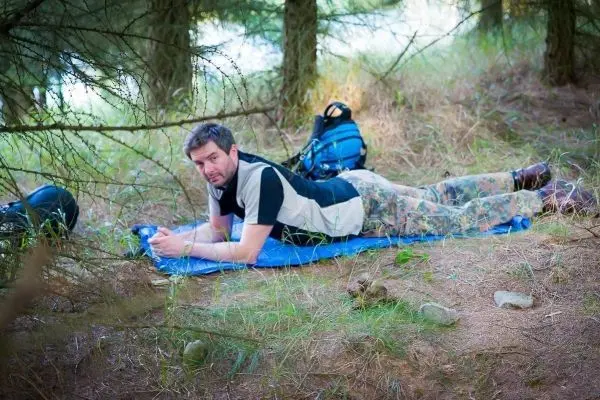 Mann liegt auf einer blauen Unterlage im Wald und schaut auf ein Gerät
