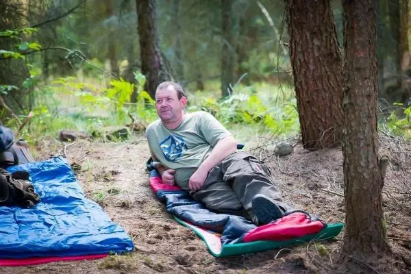 Mann liegt auf einer Isomatte im Wald zwischen Bäumen
