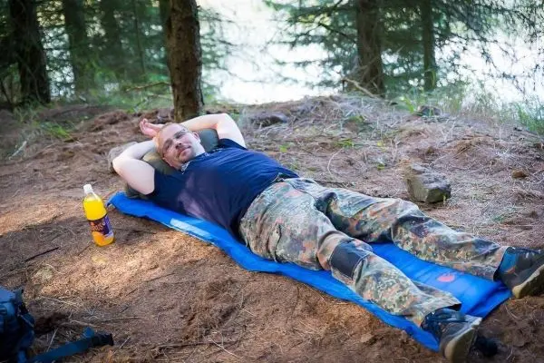 Mann liegt entspannt auf einer blauen Isomatte im Wald