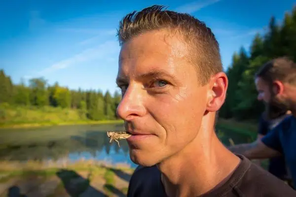 Mann mit Heuschrecke auf der Lippe steht am Ufer eines Gewässers