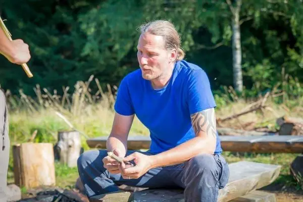 Mann sitzt auf Holzbank und hält ein Messer in der Hand