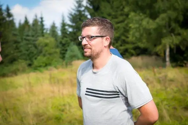 Mann steht in einer Wiese mit Bäumen im Hintergrund