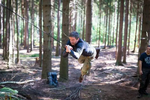 Mann überquert eine selbstgebaute Seilbrücke zwischen Bäumen im Wald
