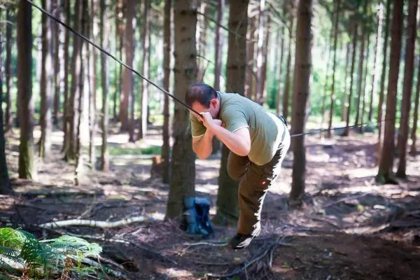 Mann überquert selbstgebaute Seilbrücke zwischen Bäumen im Wald